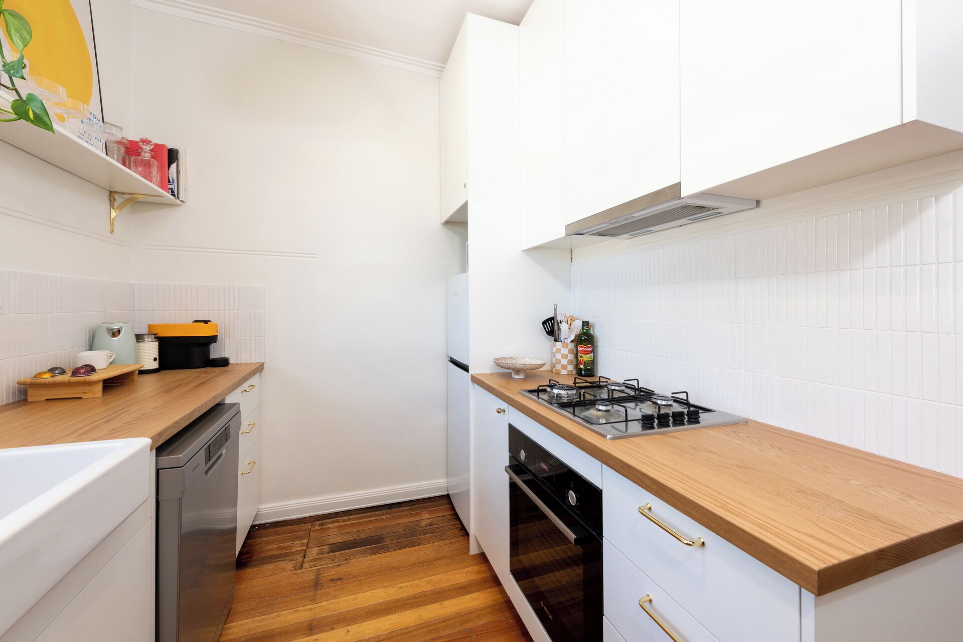 Une cuisine compacte avec des meubles blancs, un plan de travail en bois, une cuisinière à gaz et un lave-vaisselle.