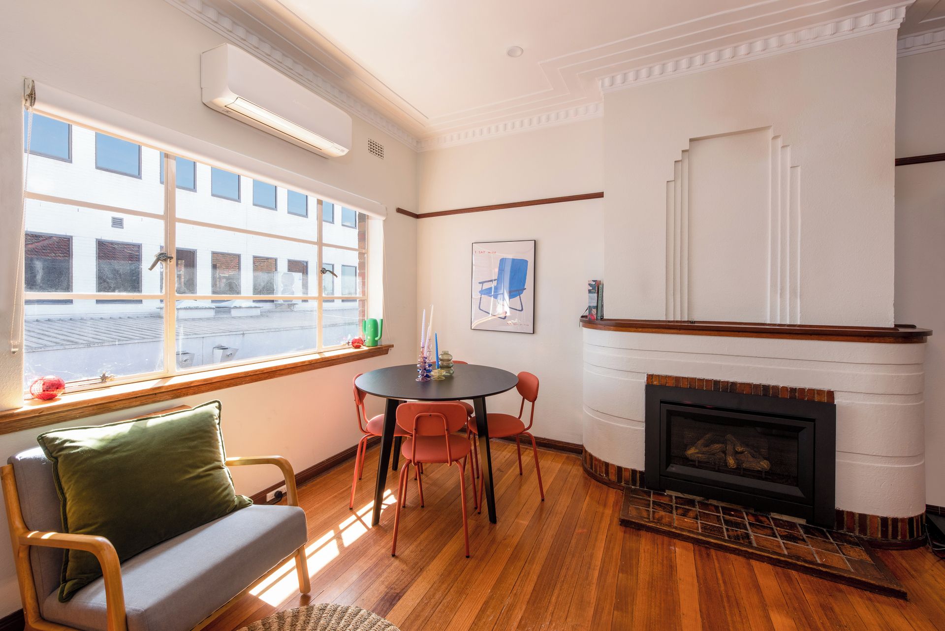 A room with a fireplace, a dining table with chairs, a sofa, and a window with a view of buildings.