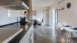 Eine moderne Küche mit einer großen Kochinsel, einem Essbereich mit Tisch und Stühlen sowie einer sichtbaren Klimaanlage.
