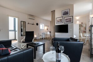 A modern living room with a sofa, a dining table, and a TV mounted on the wall. - A modern and welcoming 70-square-meter open space apartment, ideal for three people, located on the first floor of a renovated building with an elevator.The property enjoys a strategic location, just a 20-minute walk from Catania's city center and all it (Catania)
