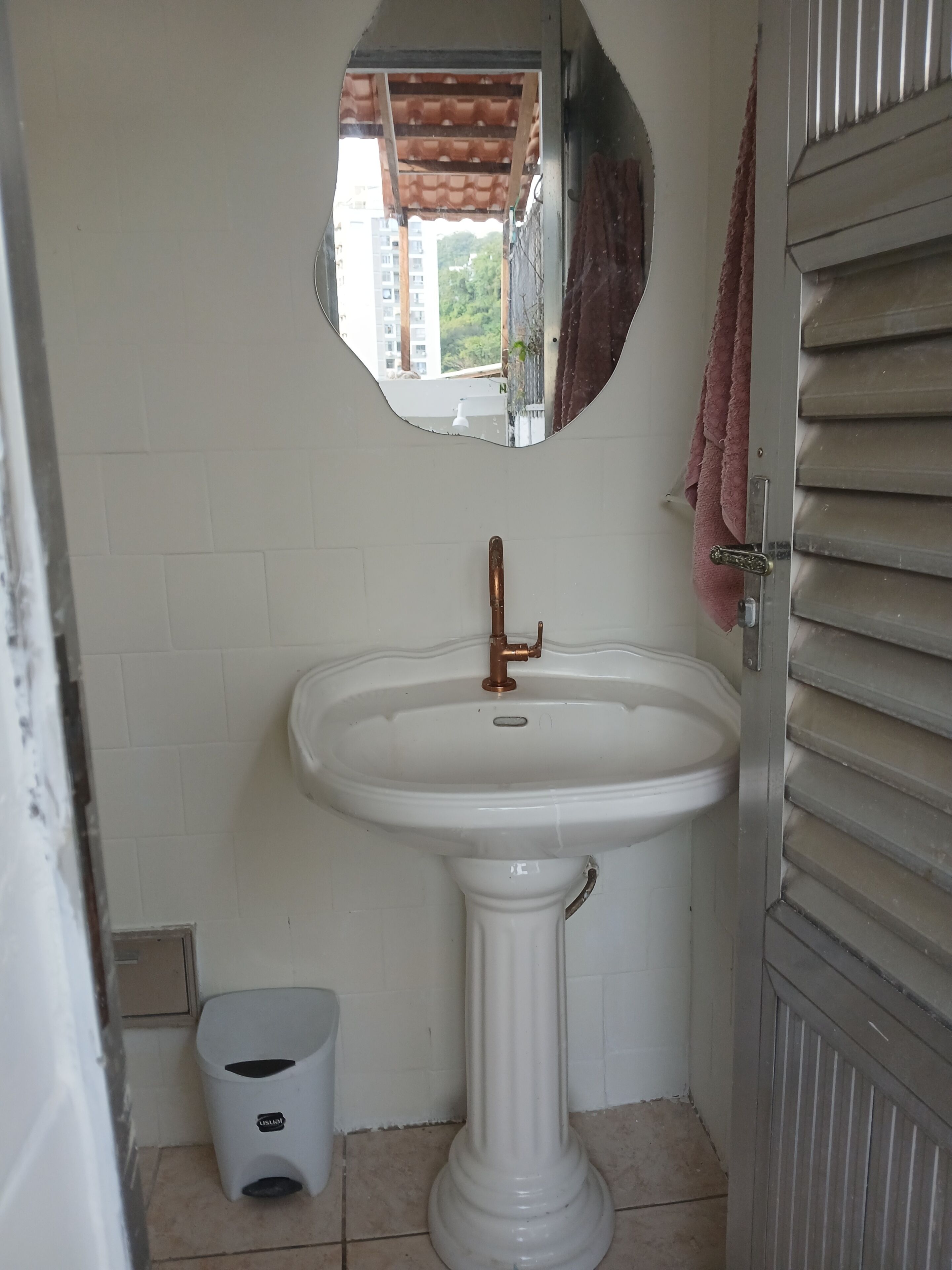 Un bagno con un lavandino bianco su piedistallo, uno specchio sopra e un asciugamano appeso alla porta.