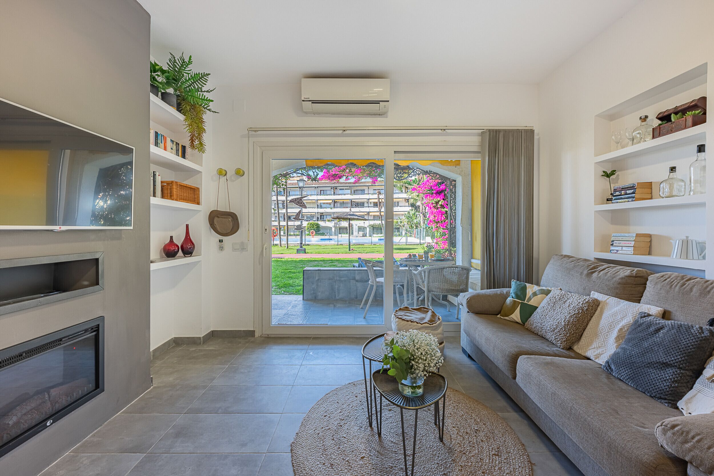 Uma sala de estar com lareira, um sofá, uma mesa de centro e vista para uma varanda com mobiliário de exterior.