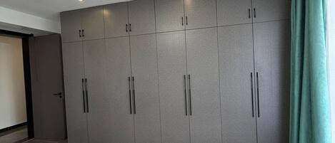 Een kamer met een grijze garderobe, een zacht wit tapijt en een blauwgroen gordijn.