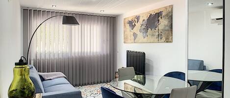 A modern living room with a sofa, a glass dining table, and chairs. There is a world map on the wall and a large mirror.