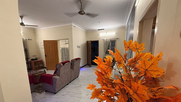 A spacious living area with a sofa, a ceiling fan, and a decorative plant. - Eden Gardens Home Stay (Coimbatore)