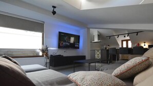 A modern living room with a flat-screen TV, a sofa, a dining table, and a kitchen area in the background. - Cozy modern apartment with a hot tub in a stone house in the heart of Omiš. (Omiš)
