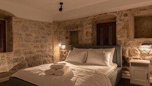 A bedroom with a stone wall, a bed with white linens, and two bedside lamps. - Cozy modern apartment with a hot tub in a stone house in the heart of Omiš. (Omiš)