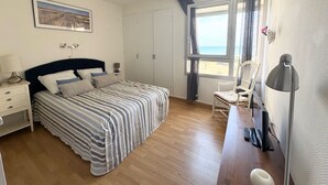 Une chambre à coucher avec un lit, un bureau, une chaise, une fenêtre donnant sur un beau paysage et un tableau accroché au mur.
