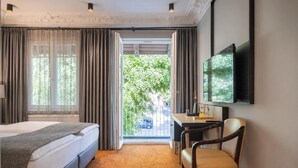 A hotel room with a bed, a desk, a chair, a TV, and a view of greenery outside. - Hotel Villa Nord (Hamburg)