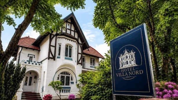 A traditional European-style building with a prominent entrance, a signboard, and lush greenery. - Hotel Villa Nord (Hamburg)