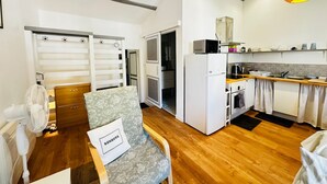 A compact kitchen with a microwave, stove, and sink, a chair with a pillow, and a fan. - Bright city centre apartment - 3 guests (Fouras)