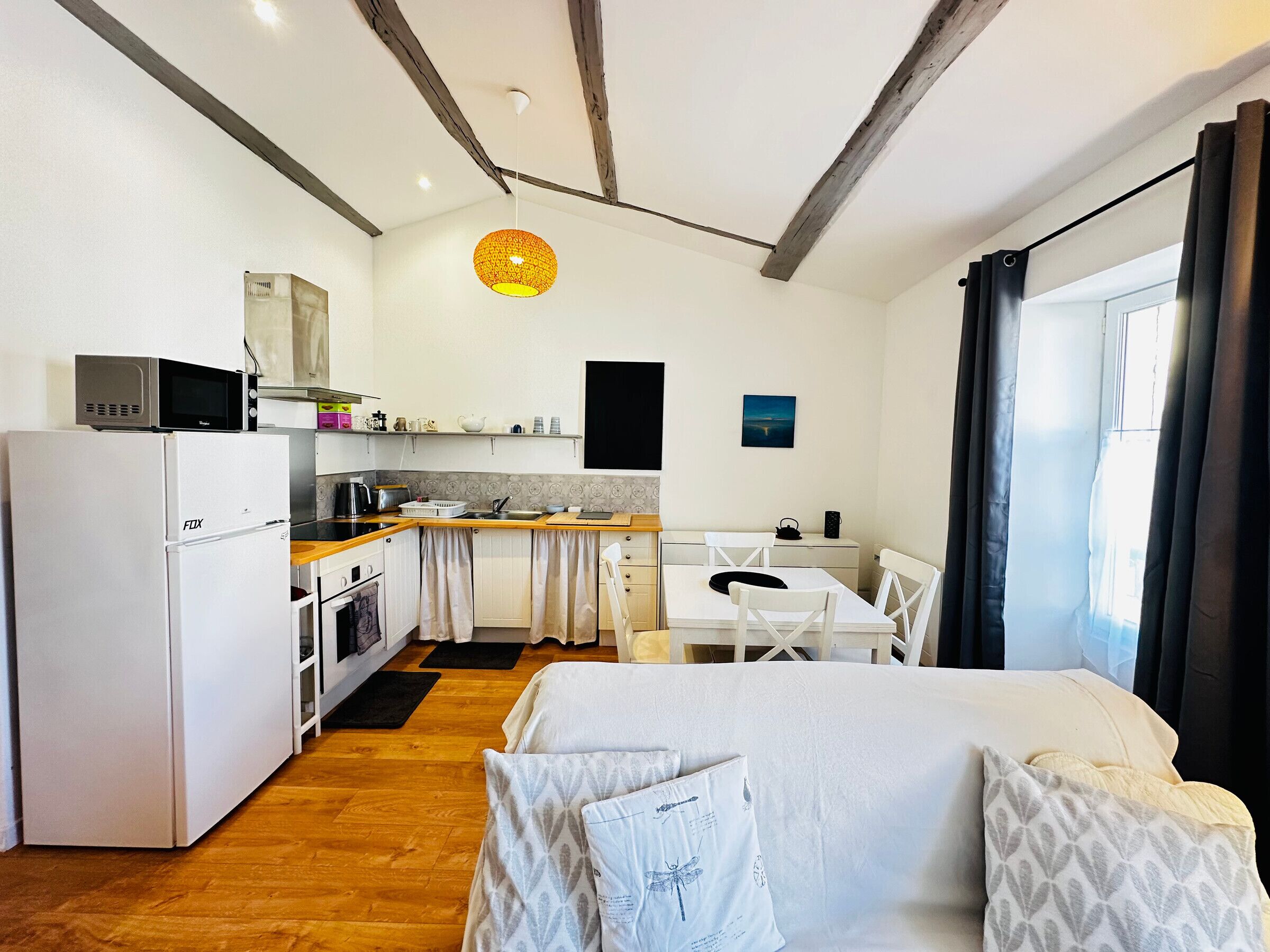 Une chambre d’hôtel compacte comprenant un coin cuisine, un espace repas et un lit agrémenté d’oreillers à motifs.