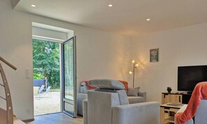 A modern living room with a sofa, a television, and a floor lamp. There is a sliding glass door leading to an outdoor area with a bench.