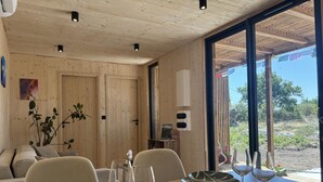 A dining area with a wooden table, chairs, and a view through large windows.