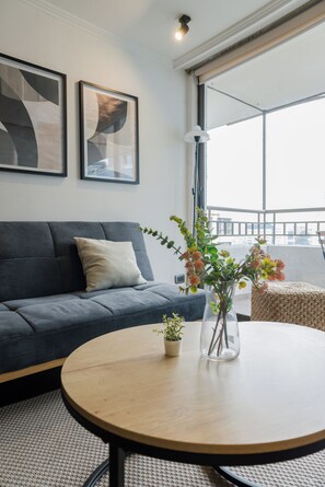 A modern living room with a grey sofa, a round wooden coffee table, and a vase with flowers. - Providencia Moderno 2D 5 huespedes (Providencia)
