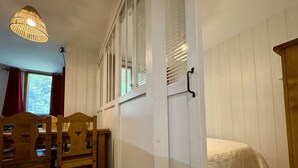 Una habitación con una cama, una mesa de madera con sillas, una lámpara colgante y un ventanal con persianas.