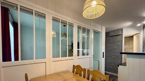 Un comedor con mesa y sillas de madera, ventanas amplias con vidrio esmerilado y una lámpara colgante.