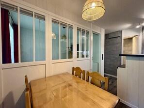 Ein Essbereich mit einem Holztisch und Stühlen, großen Fenstern mit Milchglas und einer hängenden Leuchte.