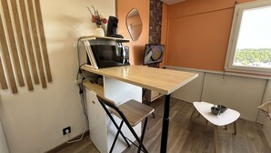 Une pièce compacte comprenant un coin cuisine, une petite table à manger, une chaise, un téléviseur et une fenêtre.