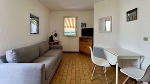A compact living space with a sofa, a small table with chairs, a TV, and a window with curtains.