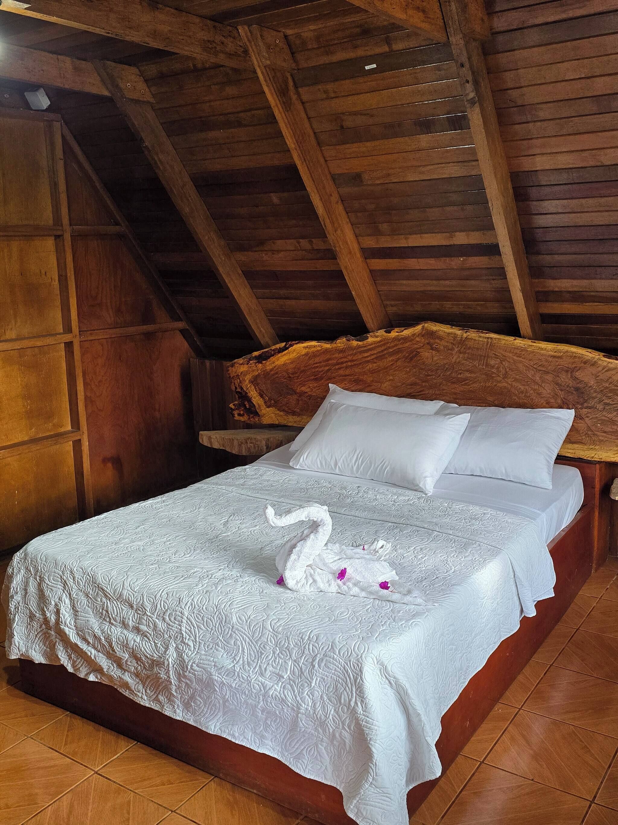 A wooden ceiling with exposed beams, a bed with white linens and a swan-shaped pillow, and a wooden headboard.