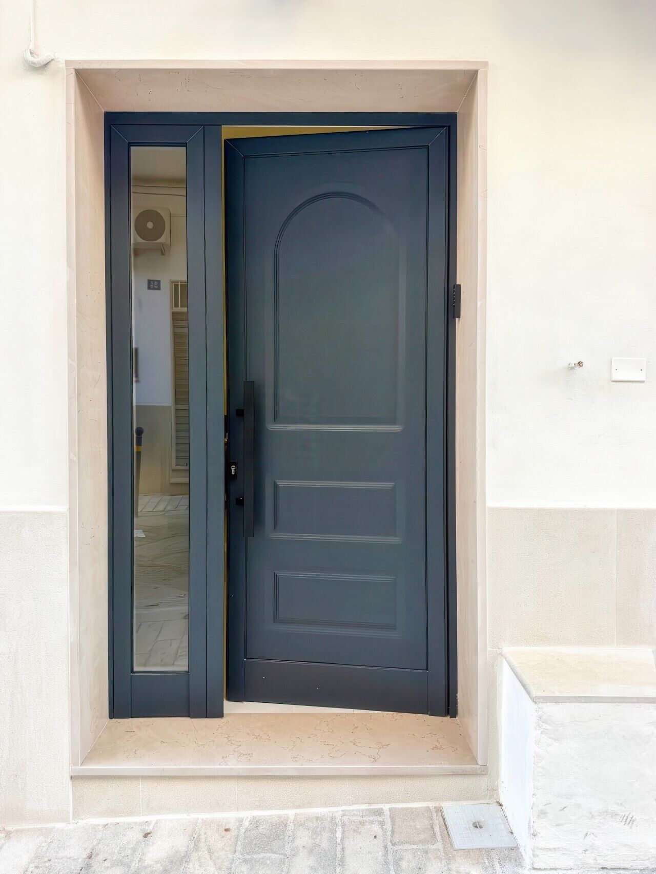 A dark-colored door with a glass panel, a small step leading up to it, and a light-colored wall.
