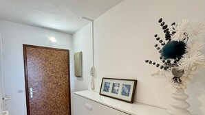 A hallway with a wooden door, a white reception desk, a framed picture, and a decorative vase. - 19 STUDIO CLIM VUE MER (Sète)