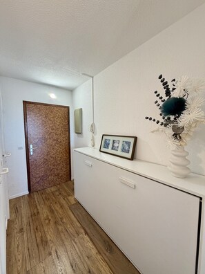 A hallway with a wooden door, a white reception desk, a framed picture, and a decorative vase. - 19 STUDIO CLIM VUE MER (Sète)