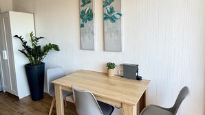 A modern kitchen with a wooden table, two grey chairs, a potted plant, and two wall-mounted paintings. - 19 STUDIO CLIM VUE MER (Sète)