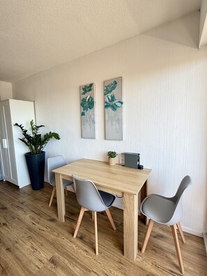 A modern kitchen with a wooden table, two grey chairs, a potted plant, and two wall-mounted paintings. - 19 STUDIO CLIM VUE MER (Sète)