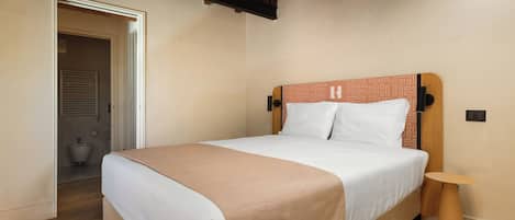 A bedroom with a bed, a bedside table, a wooden headboard, a door leading to a bathroom, and a small round table.