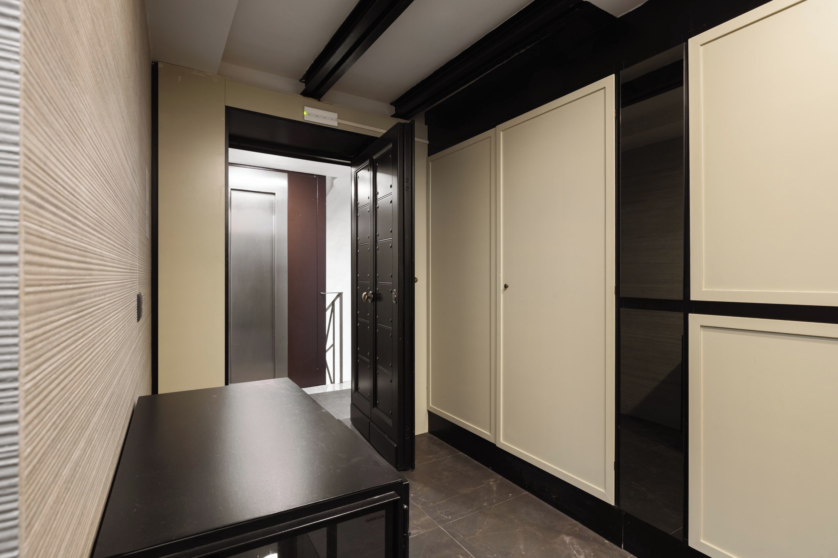 A hallway with a black table, a wardrobe with a mirror, and a door leading to another room.