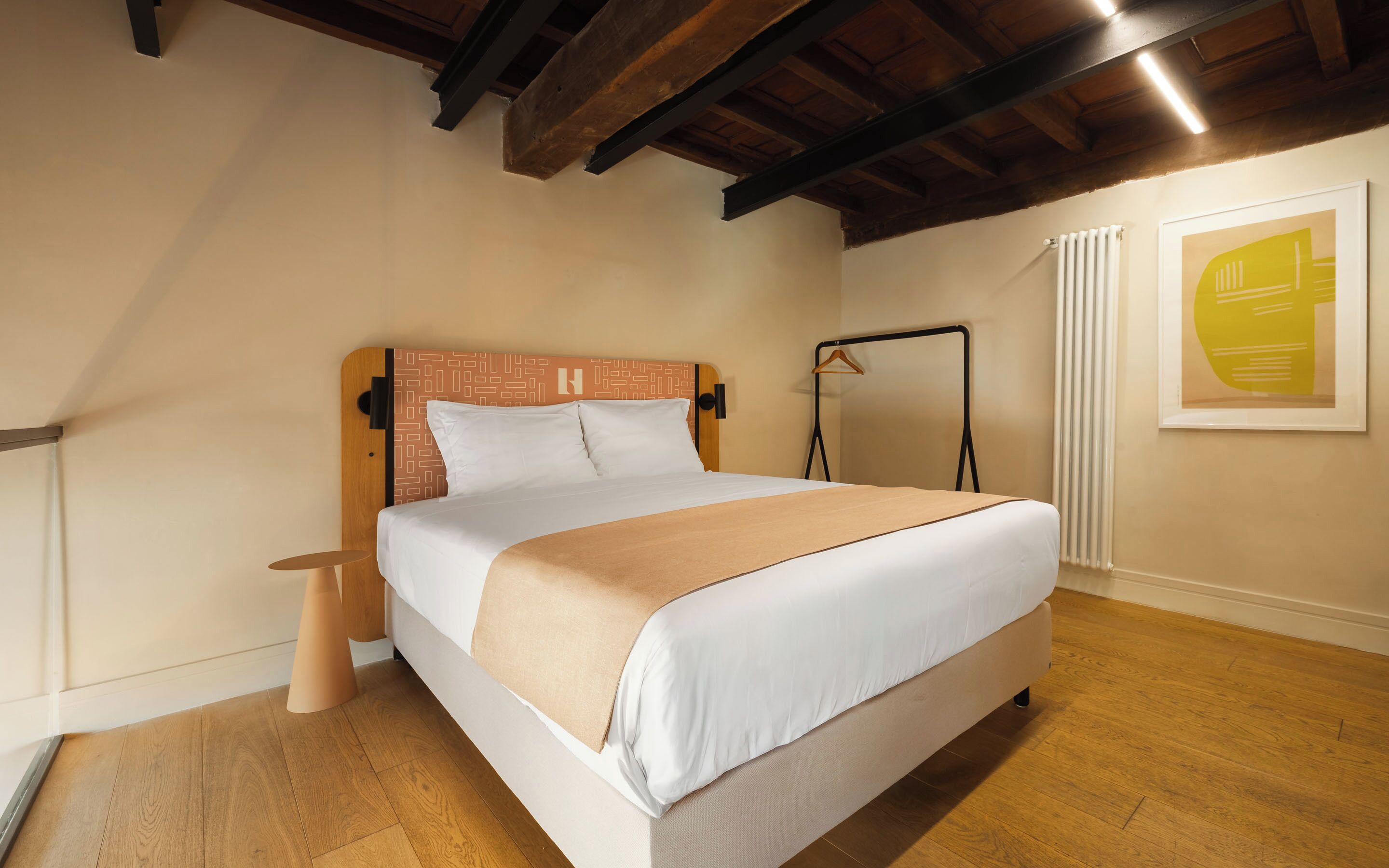 A bedroom with a bed, wooden floor, a radiator, and a framed abstract painting.