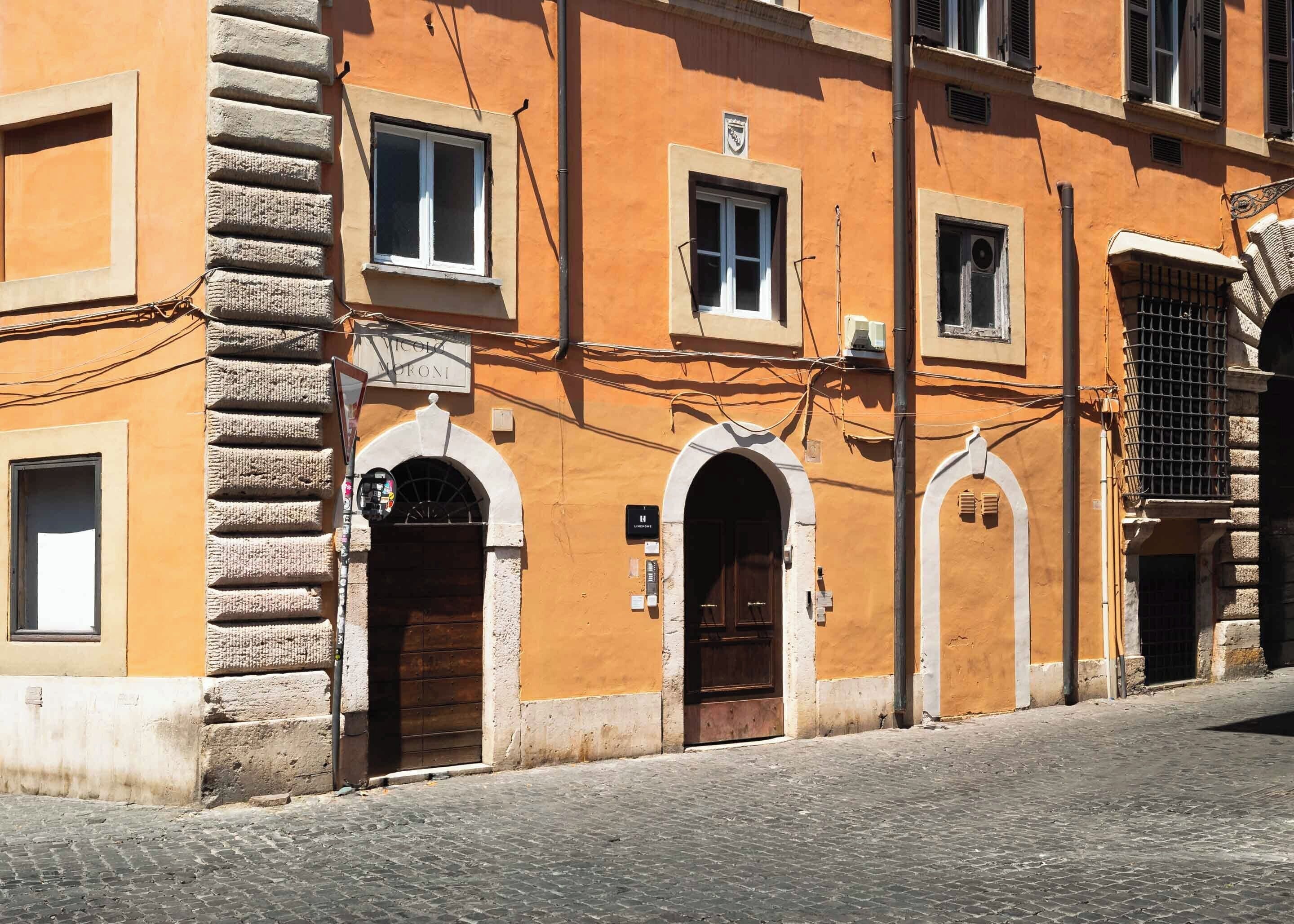 Um edifício com várias portas e janelas em arco, rua de calçada e uma placa sobre a entrada.