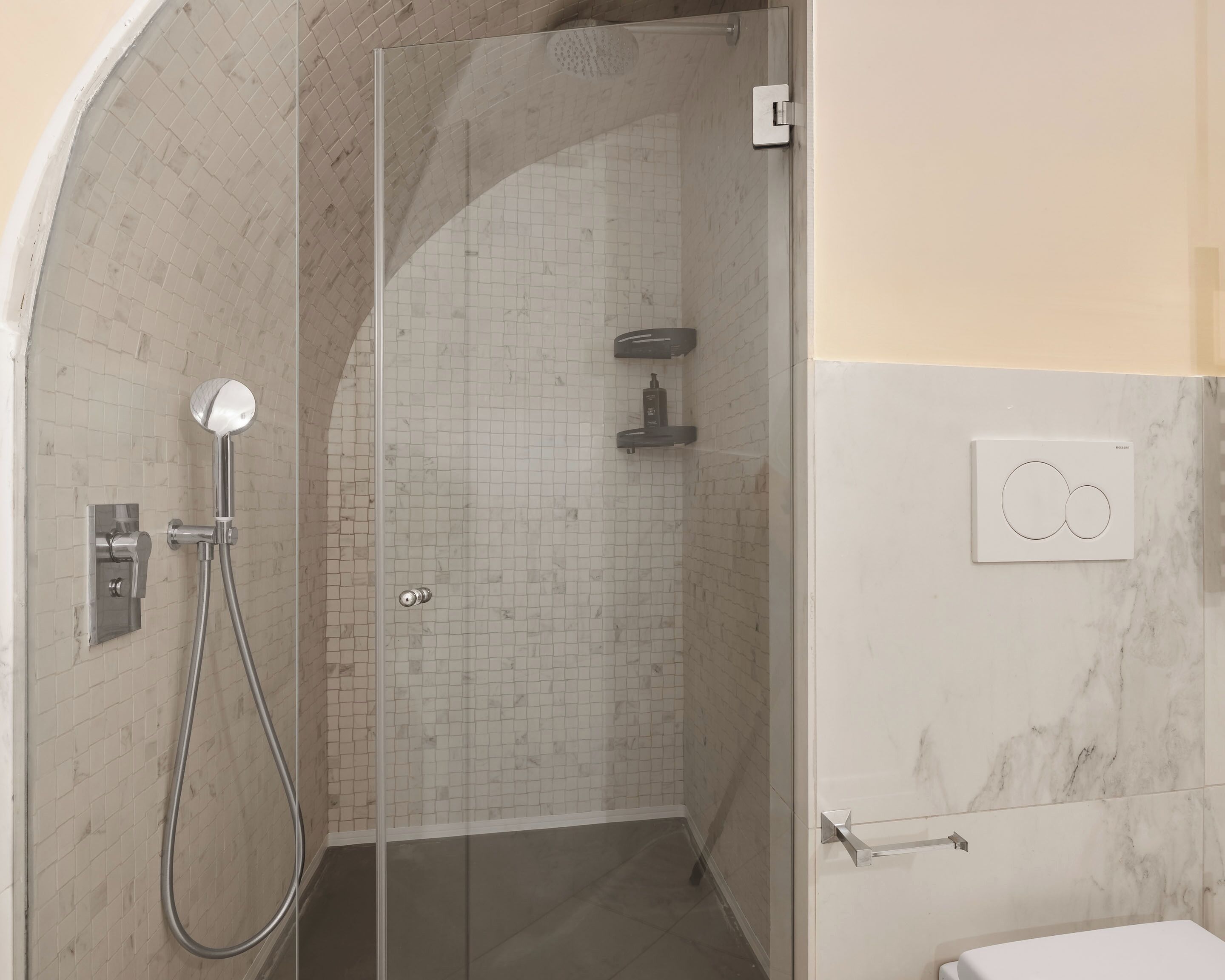 A glass-enclosed shower with a handheld showerhead, a wall-mounted faucet, and a control panel.