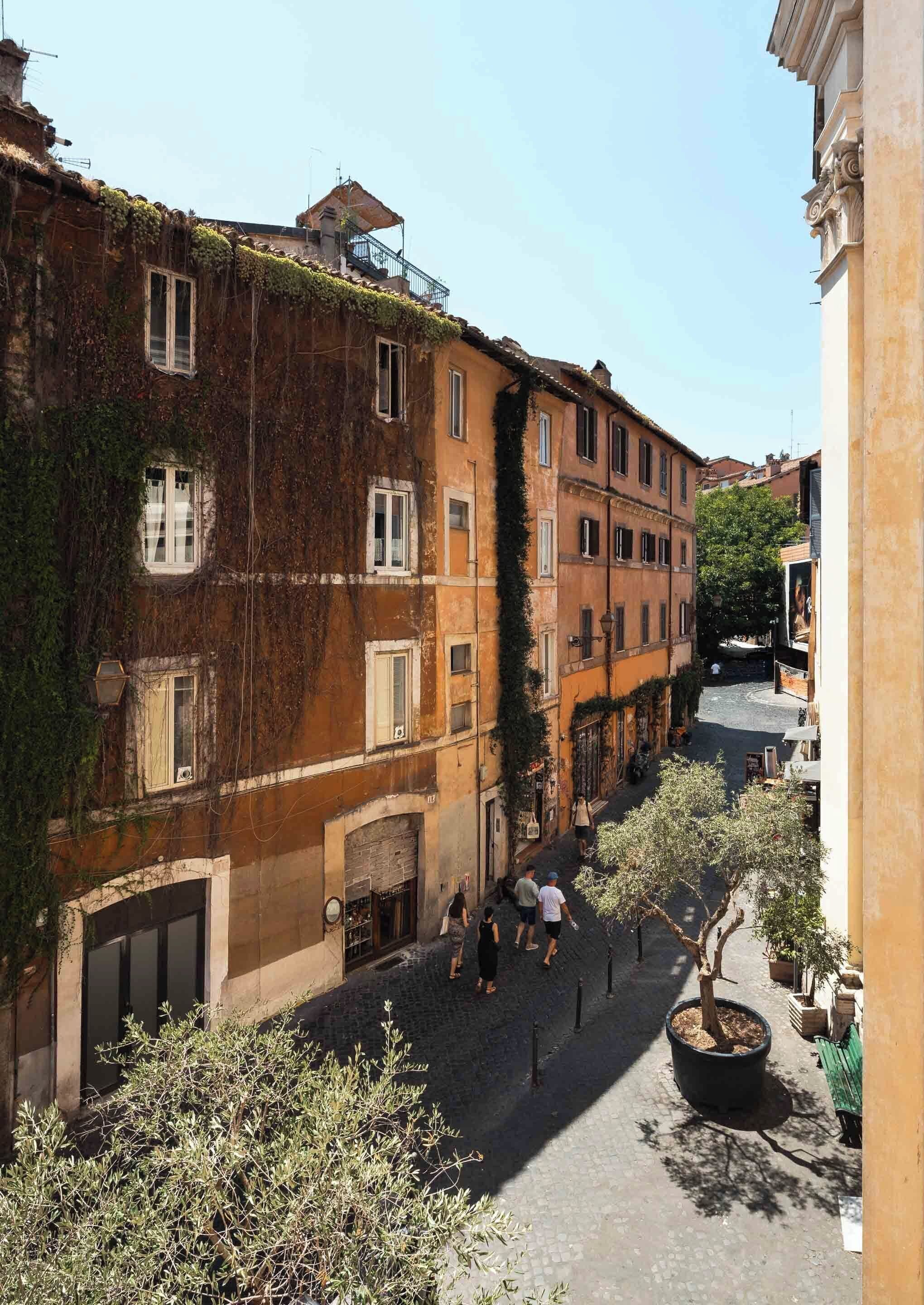 Una calle estrecha flanqueada por edificios, algunos cubiertos de hiedra, y algunas personas caminando.