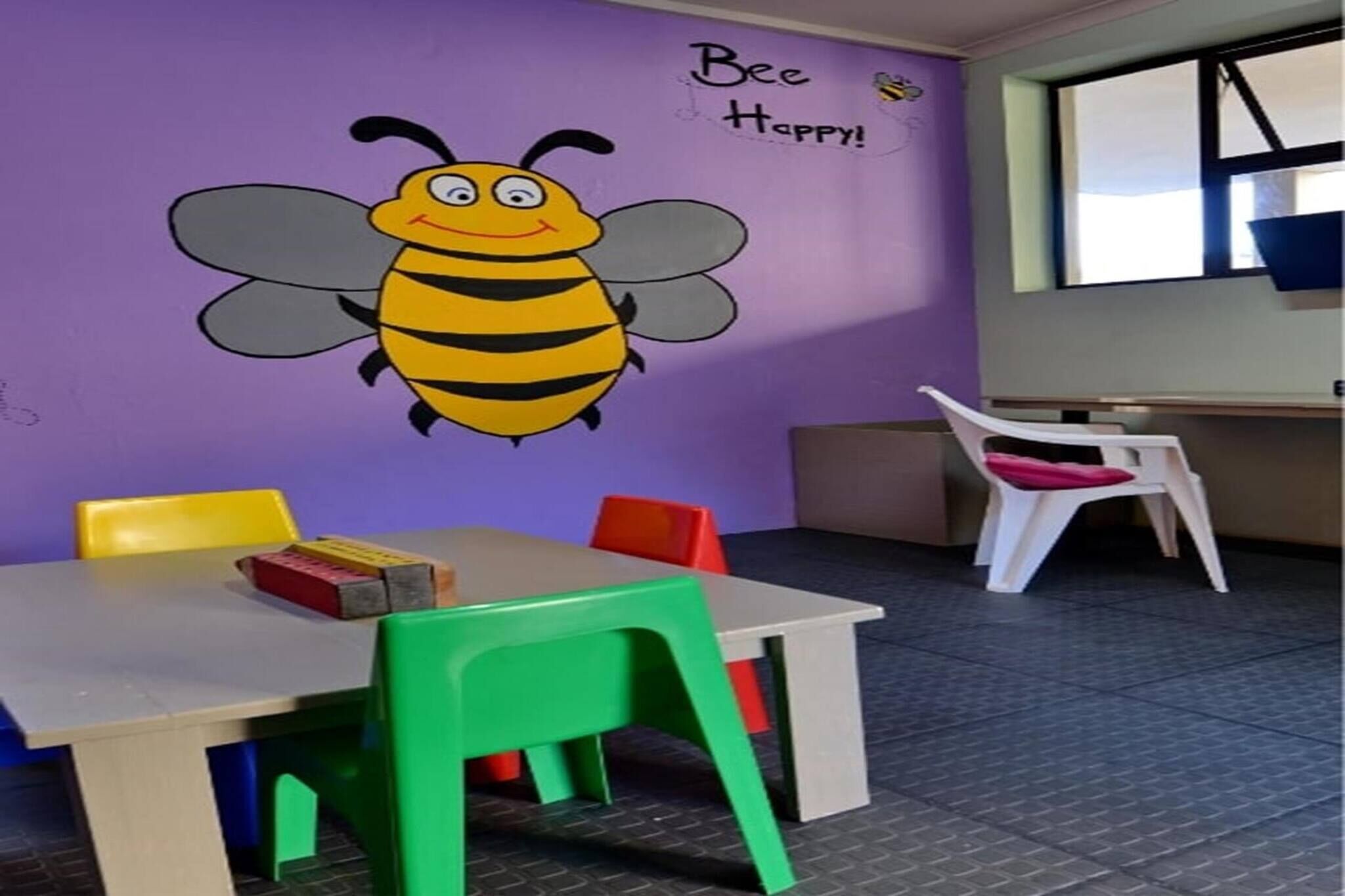 A room with a purple wall, a bee mural, a table with chairs, and a window.
