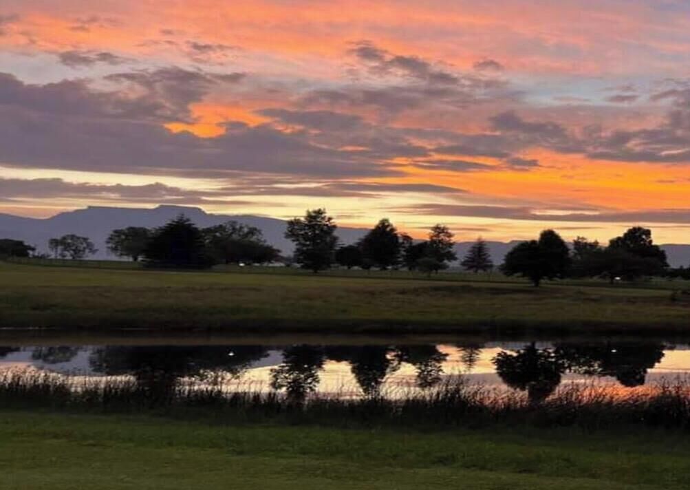 A landscape with a body of water reflecting the sky, trees, and distant mountains.