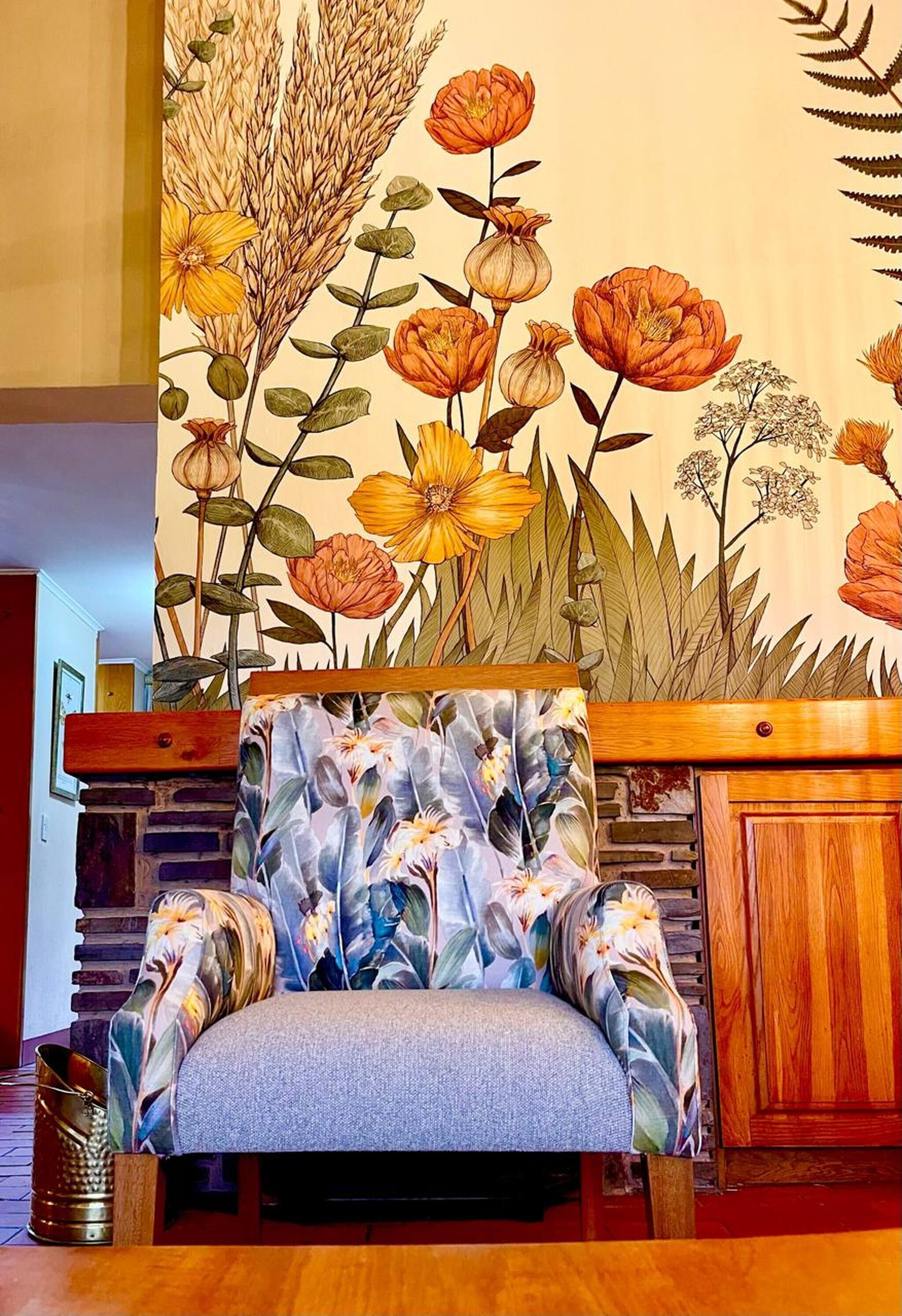 Una silla con estampado floral, un aparador de madera y una pared con un gran mural floral.