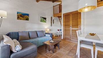 Una sala de estar acogedora con sofá, una mesa de centro y una mesa de comedor con sillas. Se ve una escalera que sube a un nivel superior.