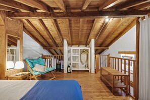 Un dormitori tipus altell de fusta amb un llit, una cadira penjant i una escala de fusta.