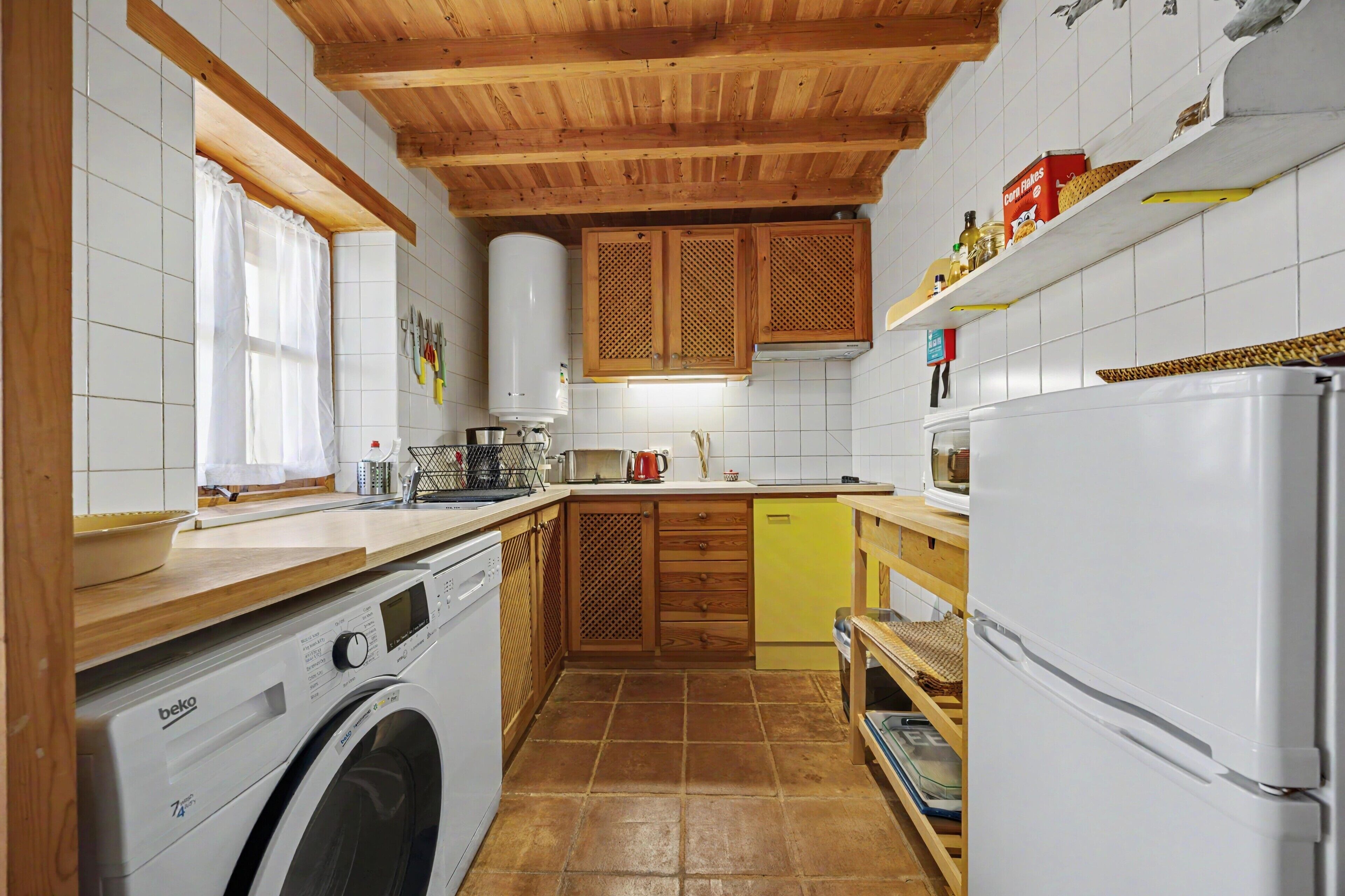 Cocina compacta con armarios de madera, lavadora y refrigerador.