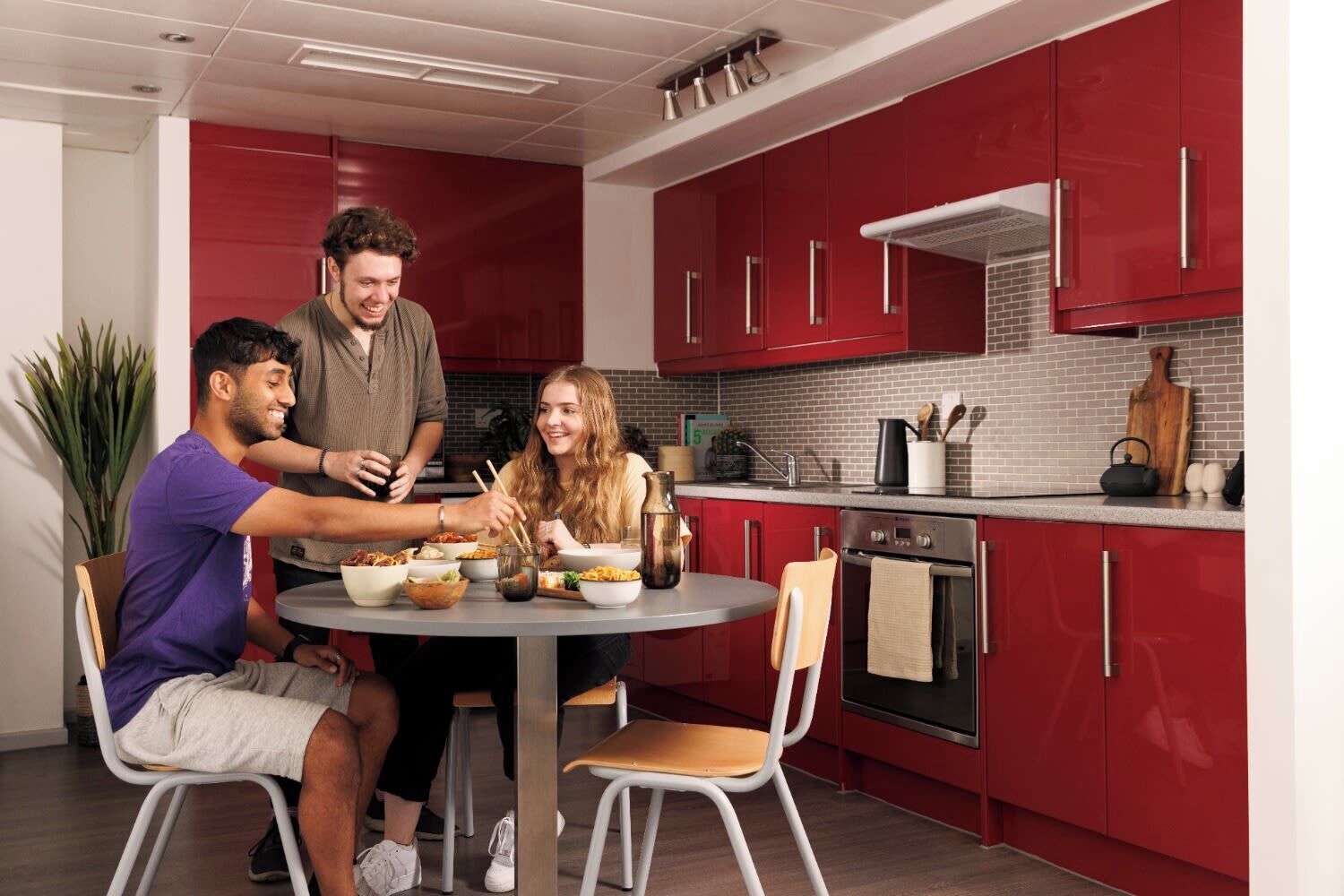 A modern kitchen with red cabinets, a round dining table, and a person serving food.