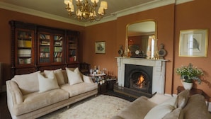 Ein Wohnzimmer mit einem beigen Sofa, einem Kamin, einem Bücherregal und einer Chandelier.