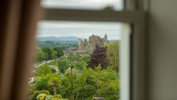 Blick auf eine historische Burg, umgeben von üppigem Grünwerk, durch ein Fenster hindurch.