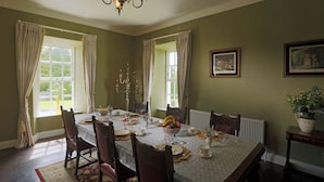 Ein Esszimmer mit Tisch für vier Personen, umgeben von Stühlen, einer Deckenleuchte und einem Fenster mit Vorhängen.