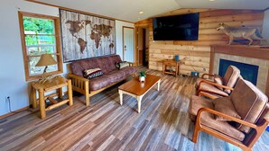 Una sala de estar con sofá, mesa de centro, sillas, televisión, chimenea y un mapa mundial pintado en la pared.