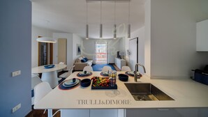 A modern kitchen with a central island, a dining area with white chairs, and a view to the outside. - TD Terrazza Giulia Monopoli City Center (Monopoli)