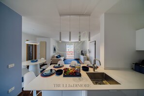 A modern kitchen with a central island, a dining area with white chairs, and a view to the outside. - TD Terrazza Giulia Monopoli City Center (Monopoli)