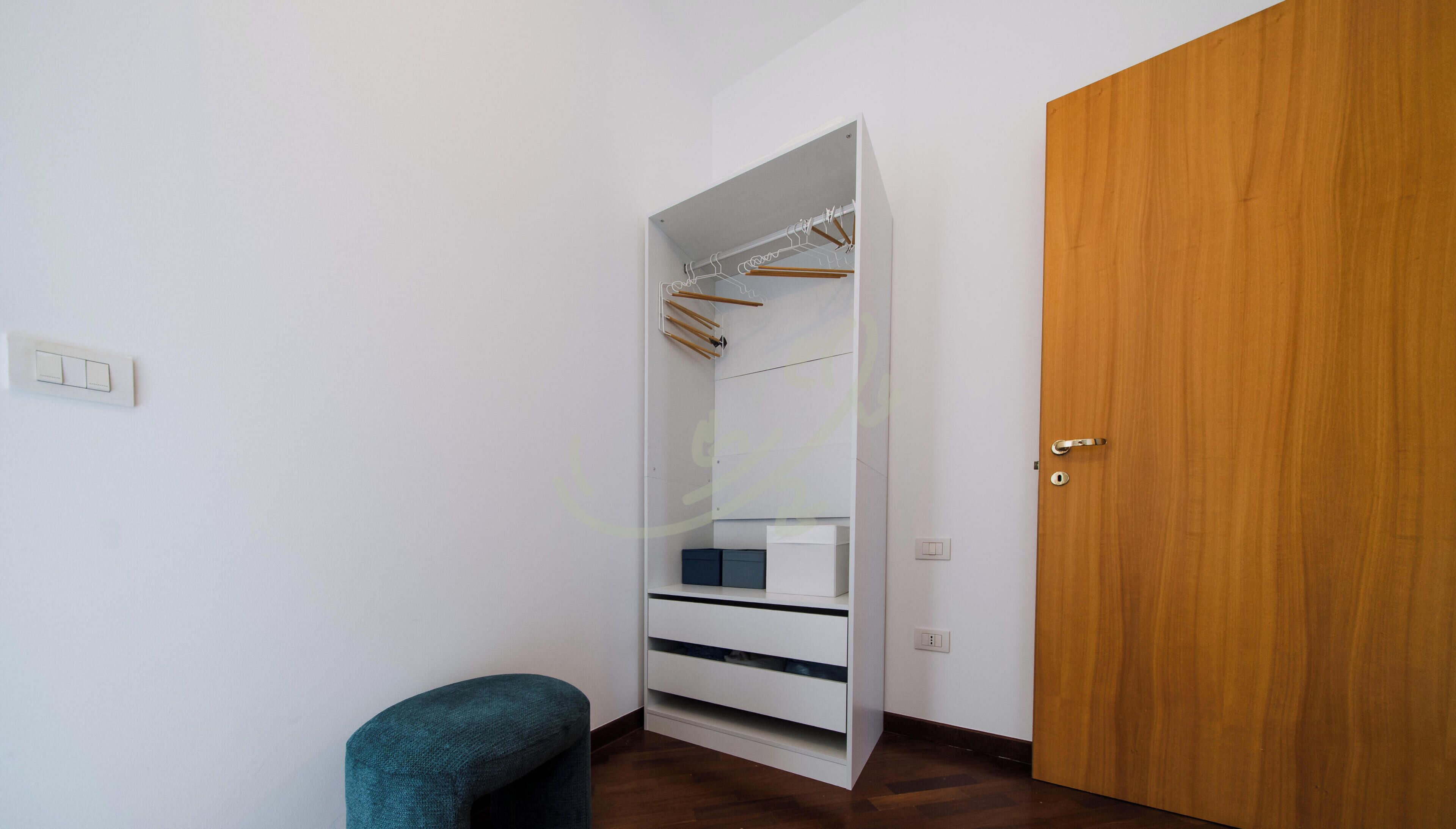 A walk-in closet with hanging space and drawers, a wooden door, and a small chair.